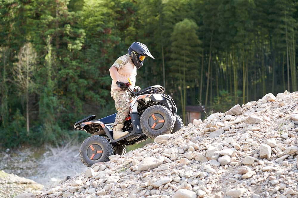 Rider standing on the footboards climbing a steep gravel slope &mdash; work ATV traction and control